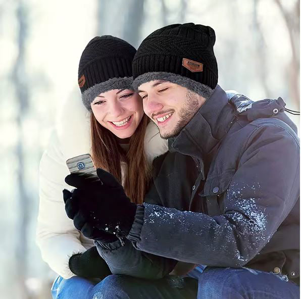 Two people wearing black beanies with brand logos in a snowy setting.