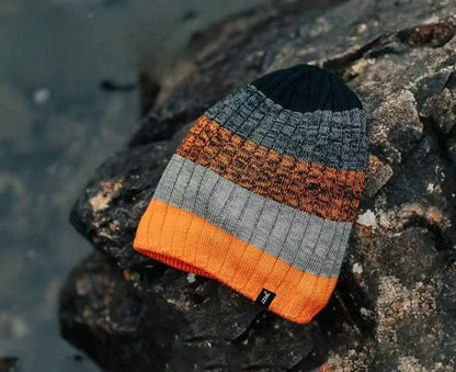 Knitted beanie with orange, grey, and black stripes on a rocky surface