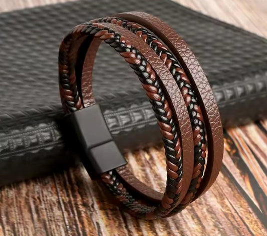Brown braided leather bracelet with a black clasp on a textured surface