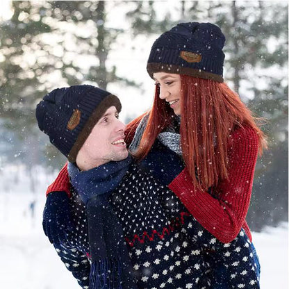 Two people hugging in a snowy forest, wearing beanies with visible brand logos.