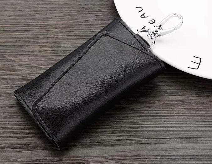 Black leather key case on a wooden surface with a white plate in the background