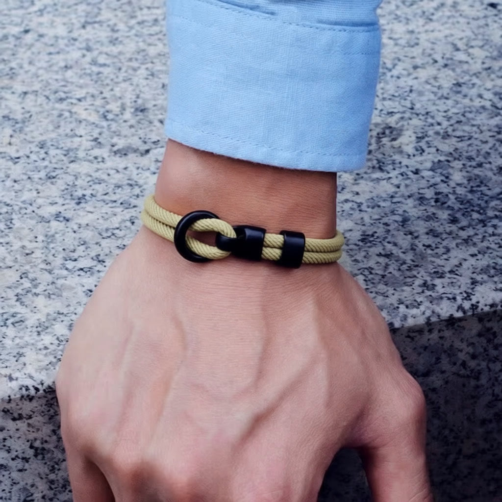 Hand wearing a khaki and black bracelet on a textured surface