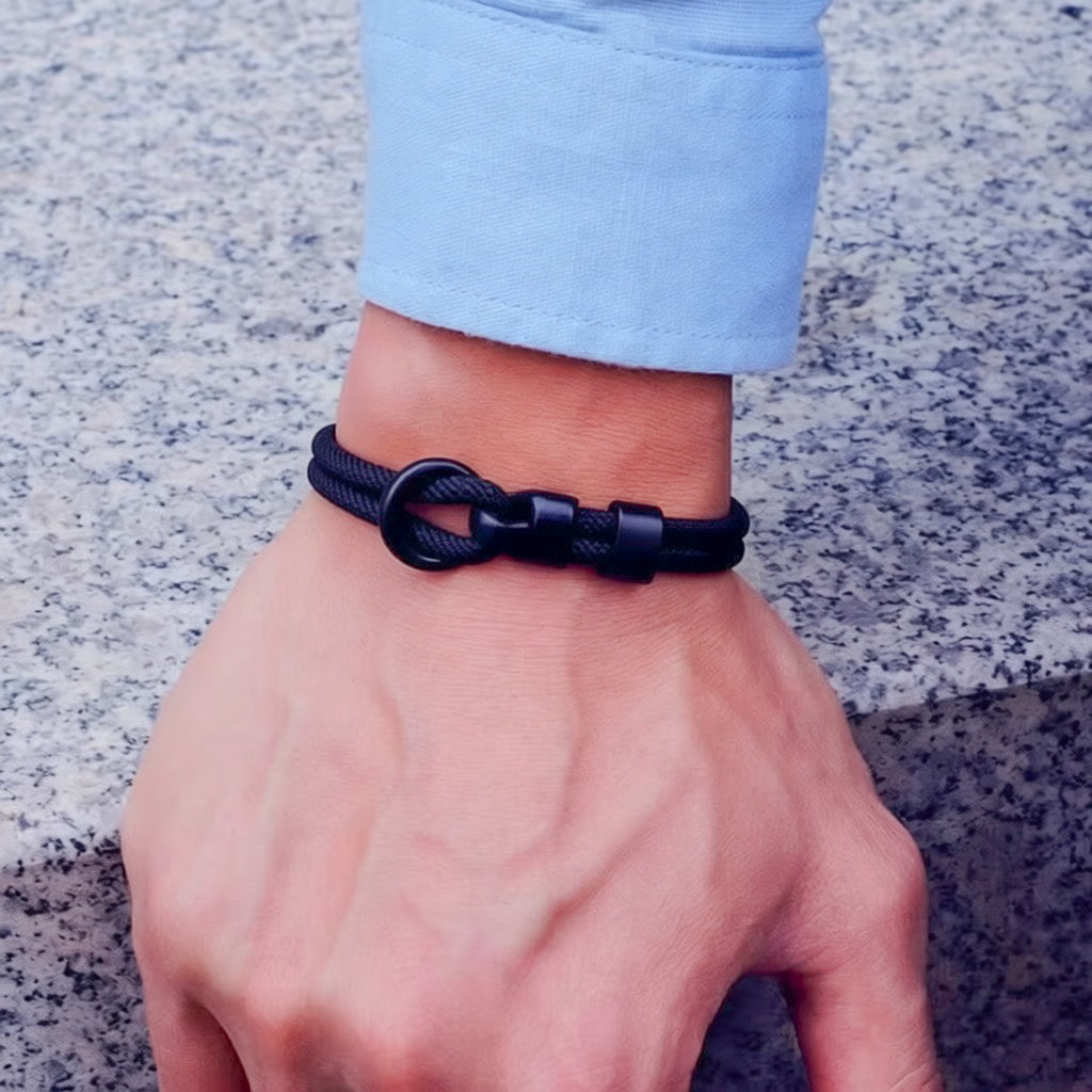 Black braided bracelet on a wrist with a light blue sleeve against a stone background