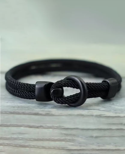 Black braided bracelet with a knot design on a light wooden surface